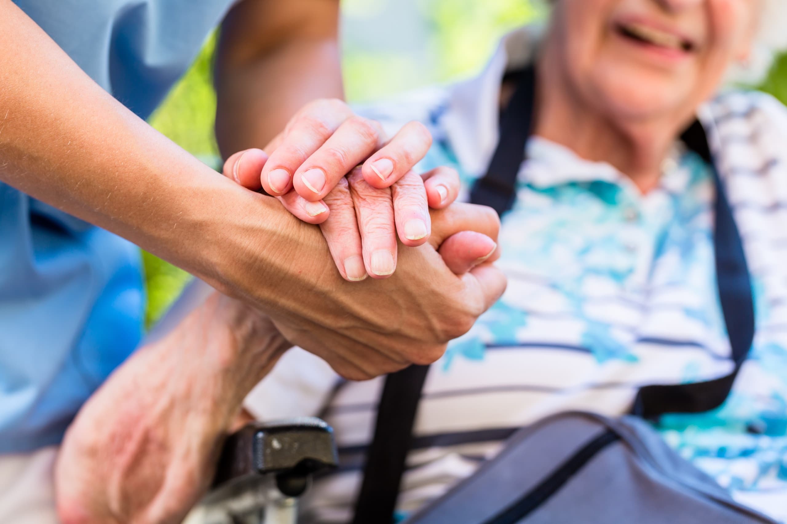 A caregiver holding the hand of a smiling older woman seated in a wheelchair